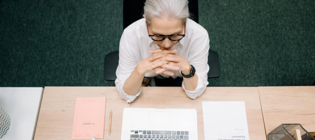 woman with gray hair and glasses sitting at desk with laptop